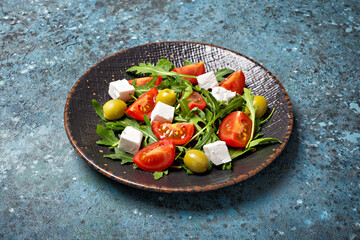 Healthy vegetarian salad with fresh arugula, cherry tomatoes, soft cheese and olives