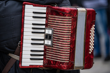 The old rare red accordion hanging on back of an accordion musician. Buttons and keyboard close up view.