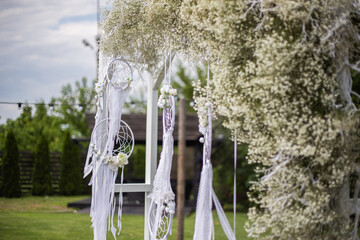 Wedding ceremony with arch with flowers and white macrame in rustic style. Wedding decoration and details
