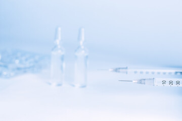 syringe with vaccine for injection and a drop at the end of the needle against the background of ampoules