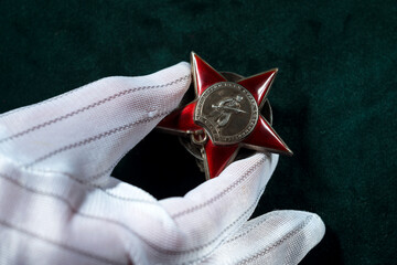 Red Star Order of the World War two in the hand of Expert wearing white canvas gloves against green...