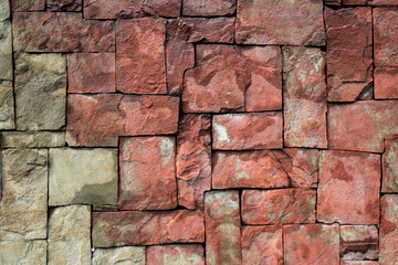 Wall of square stones of different sizes. Rectangular tiles of different sizes made of natural red stone