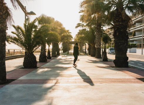 Chica montando en skate en un paseo mar&iacute;timo al atardecer