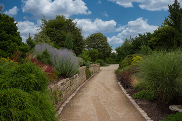 Walk in the park, beautiful landscaped garden with colorful flowerbeds under cloudy blue sky