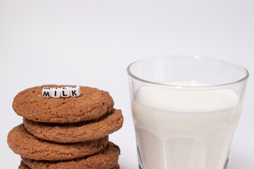 glass of milk near oat cookies with a sign MILK written with white little cubes isolated on white background. healthy breakfast snack