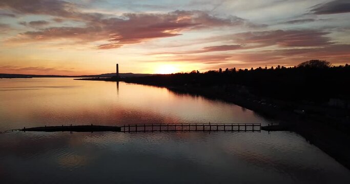 4k aerial footage of Culross Pier, Longannet power station tower and lights of Grangemouth during a spectacular sunset over the Firth of Forth, Scotland.