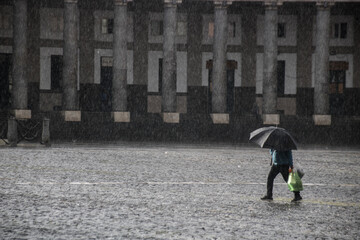 personne sous une forte averse de pluie avec un parapluie sur une place pavée