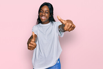 Young african american woman wearing casual white t shirt approving doing positive gesture with hand, thumbs up smiling and happy for success. winner gesture.