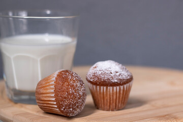 two little cupcakes or muffins in powdered sugar near a glass of milk. healthy breakfast. snack or lunch