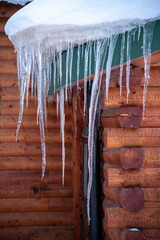 Dangling long icicles seen on the side of a stunning log cabin, home, house building with sharp edges in winter time season. 