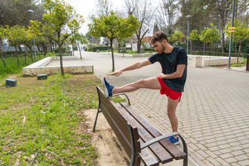 Young athlete using bench for stretching after doing workout in the park.