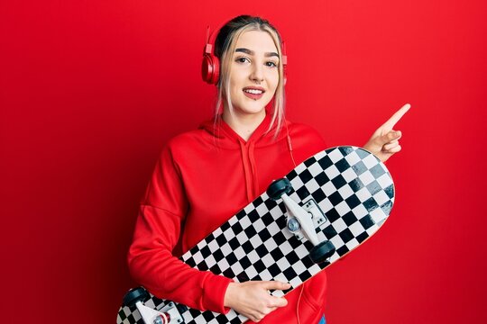Young modern girl holding skate wearing headphones smiling happy pointing with hand and finger to the side