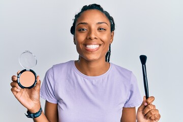 African american woman holding makeup brush and blush smiling with a happy and cool smile on face....