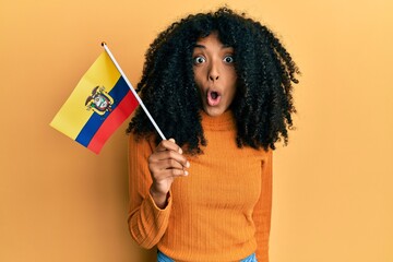 African american woman with afro hair holding ecuador flag scared and amazed with open mouth for surprise, disbelief face