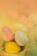 Three colored eggs in a basket and a transparent yellow cloth. Orange blurred background. Religious holiday Easter. Copy space