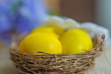 Easter sweet yellow eggs in a small nest. Blurred background of purple flowers. Shallow depth of field. Close-up