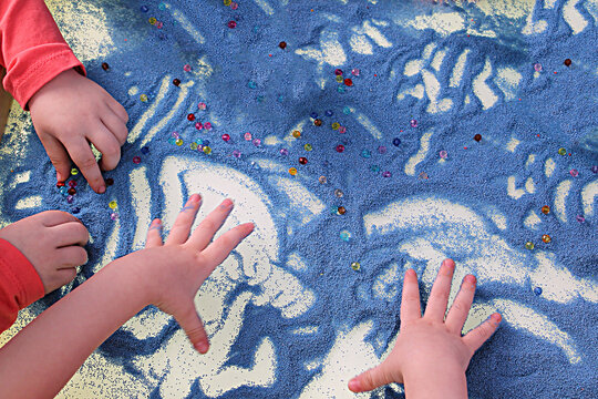 childrens hands touching blue sand on white table sand therapy, development of fine motor skills