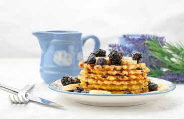 stack of baked Belgian waffles on a round plate with berries on a white table