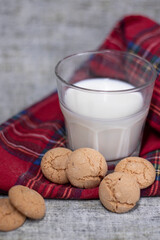 glass of milk near almond amaretti cookies on plaid red fabric tablecloth. healthy breakfast snack