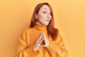 Beautiful redhead woman wearing casual winter sweater over yellow background hands together and fingers crossed smiling relaxed and cheerful. success and optimistic