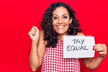 Middle age beautiful woman holding pay equal paper screaming proud, celebrating victory and success very excited with raised arm