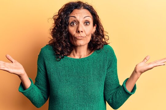 Middle age beautiful woman wearing casual sweater clueless and confused with open arms, no idea and doubtful face.
