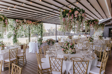 Gold chairs and tables decorated with natural pink and green flowers, candles and gold frames. Hanging flower beds and light bulbs
Wedding decoration and decor, floristic concept