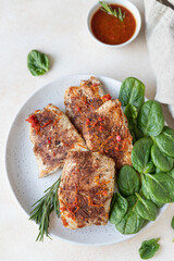 Fried turkey or chicken breast served with orange sauce, spinach and rosemary on a plate, light concrete background. Healthy balanced food.