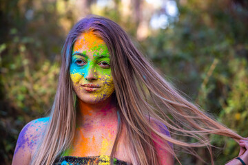 Young attractive woman at the Holi color festival of paints in park. Having fun outdoors. Multi Colored powder colors the face. Close Up portrait, people. Copy Space.