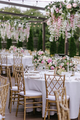 Gold chairs and tables decorated with natural pink and green flowers, candles and gold frames. Hanging flower beds and light bulbs
Wedding decoration and decor, floristic concept