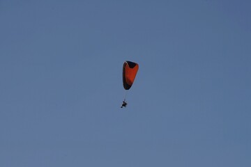 orange black paraglider with fan in blue sky