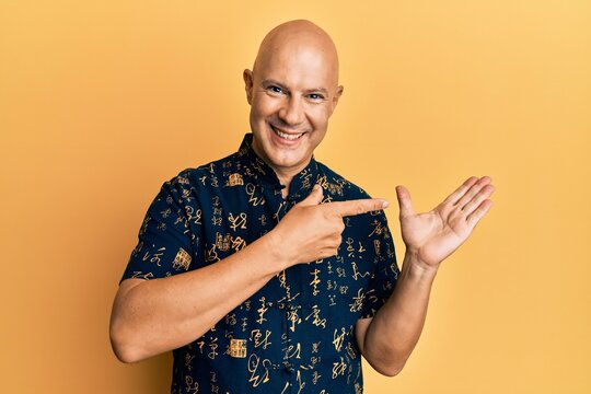 Middle age bald man wearing casual clothes amazed and smiling to the camera while presenting with hand and pointing with finger.