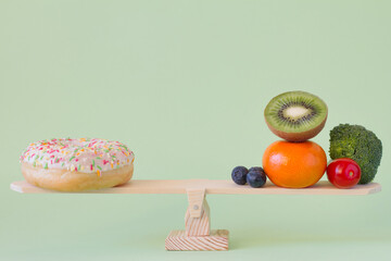 Donut vs. fruits and vegetables on wooden seesaw, diet and calories concept