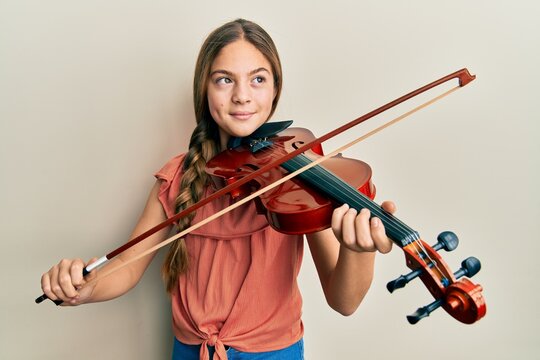 Beautiful brunette little girl playing violin smiling looking to the side and staring away thinking.