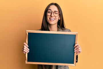 Young hispanic girl holding blackboard winking looking at the camera with sexy expression, cheerful and happy face.