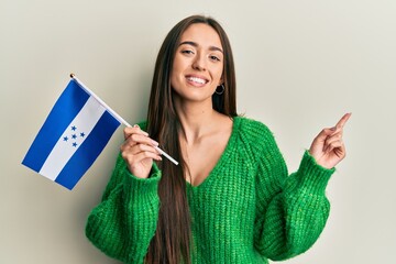 Young hispanic girl holding honduras flag smiling happy pointing with hand and finger to the side
