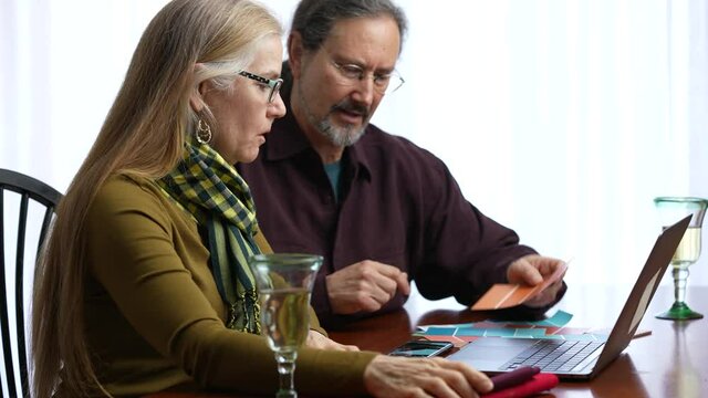 Happy smiling mature couple using laptop computer shopping house paint fabrics and talk with seniors at home.