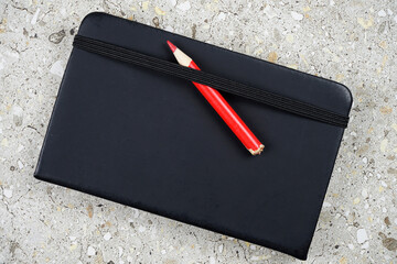 Libreta con lápiz rojo posada sobre una losa. Puede representar un simple bloc de notas, un diario...