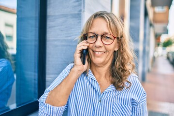 Middle age caucasian woman smiling happy talking on the smartphone at the city.