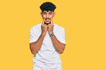 Fototapeta premium Young arab man wearing casual white t shirt smiling with open mouth, fingers pointing and forcing cheerful smile