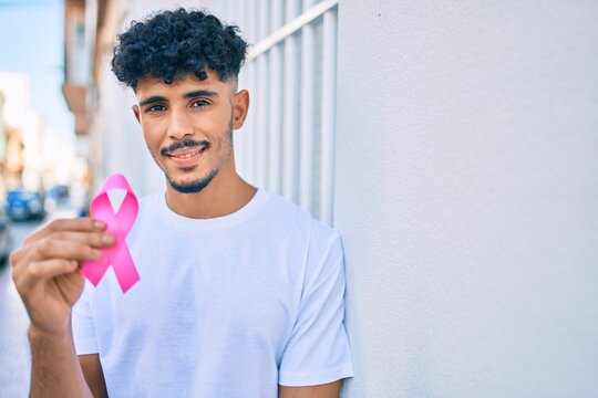 Young Arab Man Smiling Happy Holding Breast Cancer Pink Ribbon Leaning On The Wall.