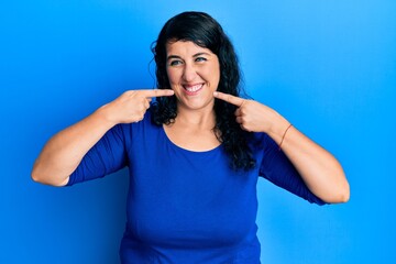 Plus size brunette woman wearing casual blue shirt smiling cheerful showing and pointing with fingers teeth and mouth. dental health concept.