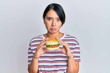 Beautiful young woman with short hair eating hamburger depressed and worry for distress, crying angry and afraid. sad expression.