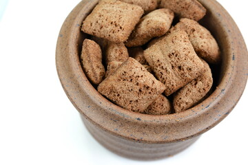 Heap of chocolate pillow cereals in a bowl isolated on white background. Nougat filled chocolate pillow wafers pile isolated on white background. Crispy chocolate cereal pillow flakes.