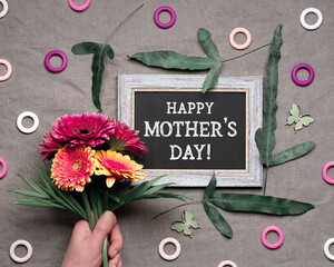 Blackboard, chalk board with text Happy Mother's Day. Tropical fern leaves around frame. Hand holds...