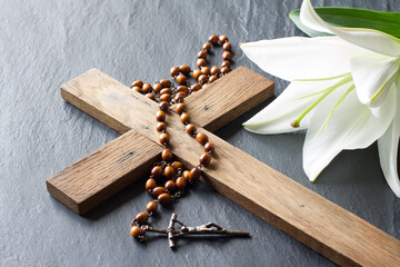 Cross, rosary and white lily on black marble background. Passion and resurrection of Christ concept 