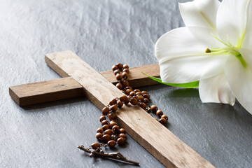 Cross, rosary and white lily on black marble background. Passion and resurrection of Christ concept 