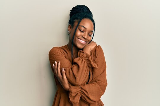 African american woman with braided hair wearing casual brown shirt hugging oneself happy and positive, smiling confident. self love and self care