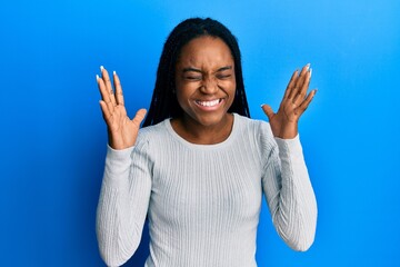 African american woman with braided hair wearing casual white sweater celebrating mad and crazy for...