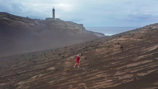 Aerial shot of man going mountain hills of Capelinhos Volcano, Faial Island, Azores, Portugal, Europe. Guy exploring island with Volcano Interpretation Center of Capelinhos on background. 4k footage